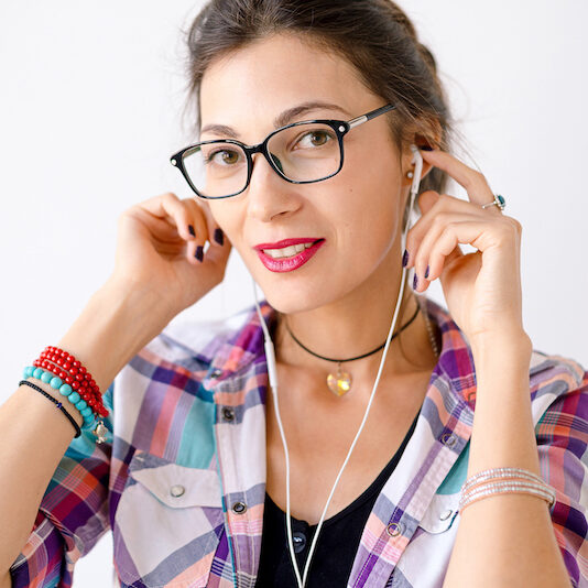 Portrait of young beautiful woman with glasses on a white background listening music holding headphones with arms, talking with somebody.
